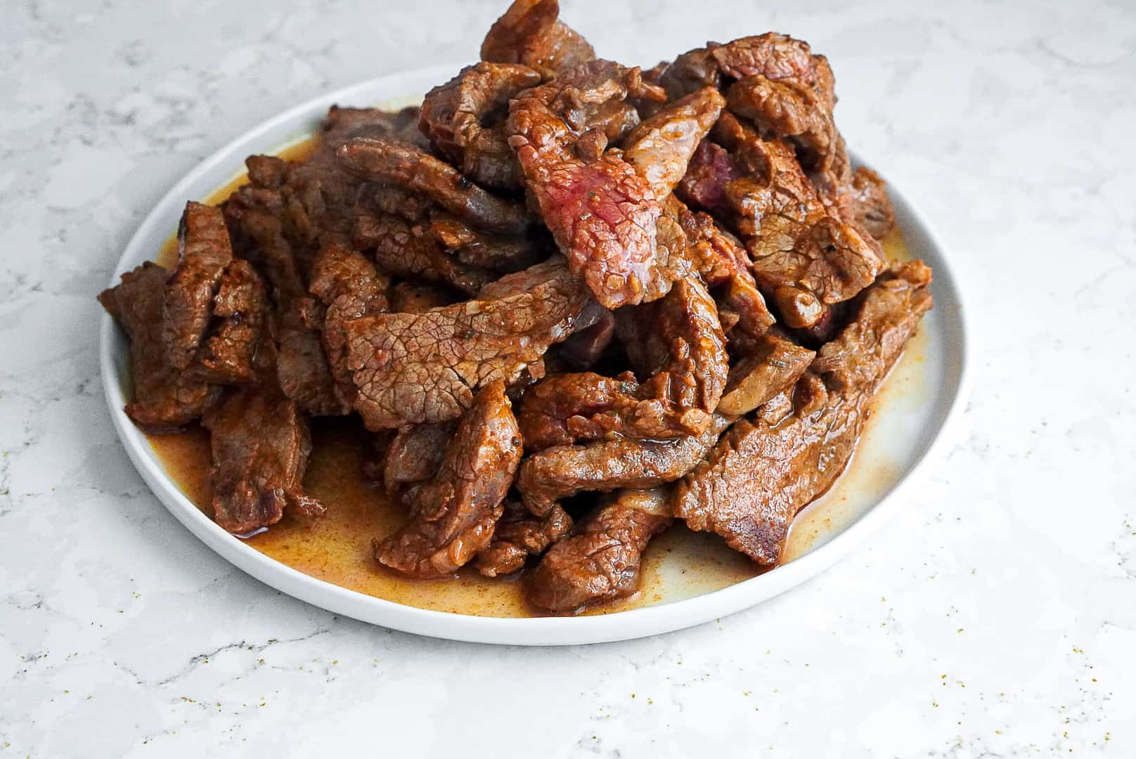 Flank steak piled high on a white plate.