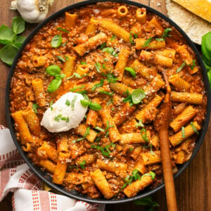 Tomato pasta with rigatoni noodles in a pan with a dollop of ricotta cheese with fresh basil and parmesan cheese on top.