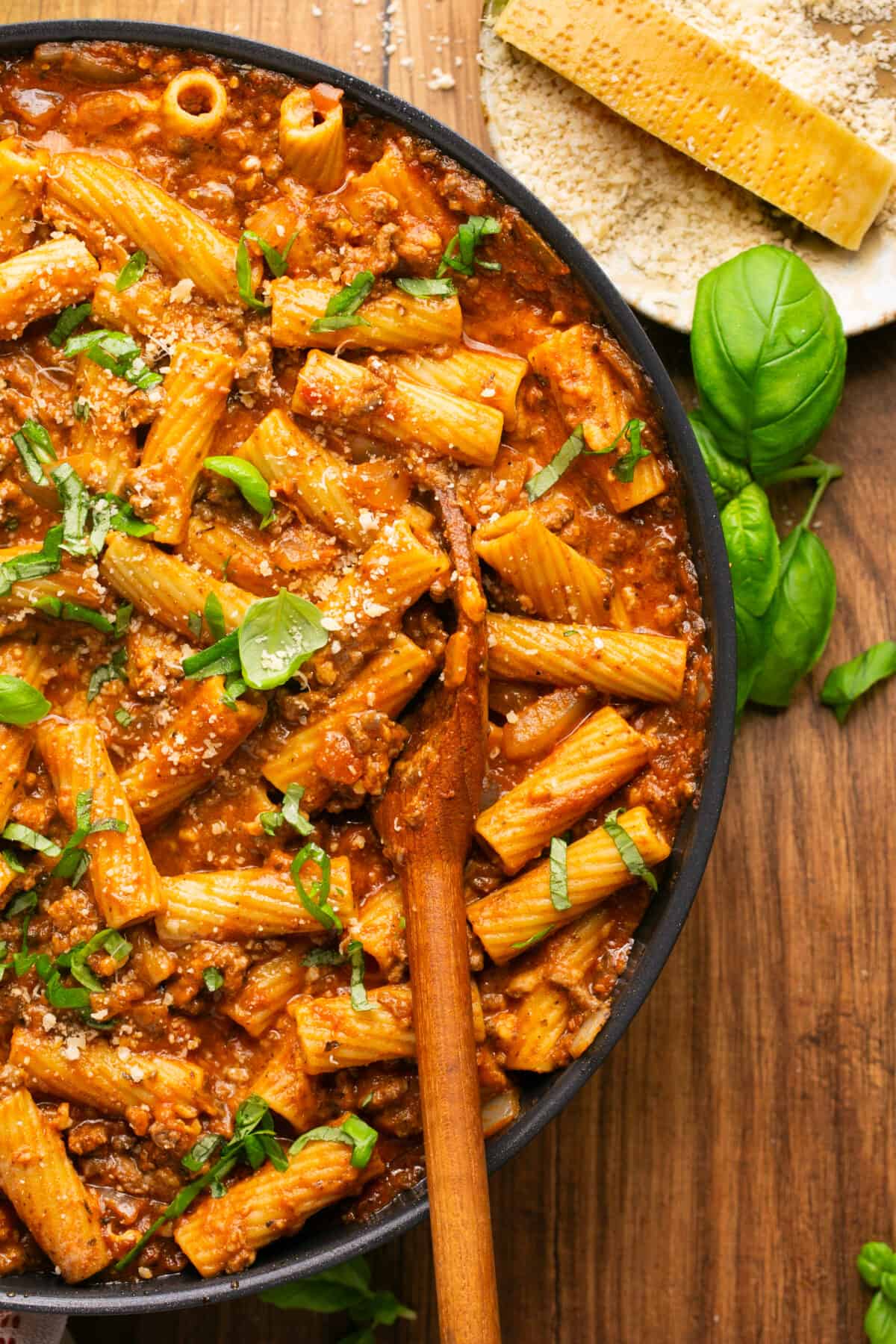 Lasagna pasta dish in a skillet with a spoon topped with fresh basil and parmesan cheese. 