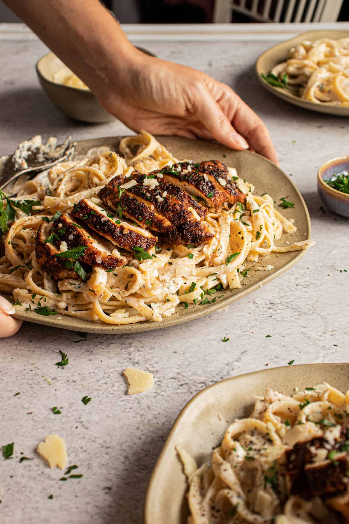 Person placing a plate of blackened chicken alfredo on a table.