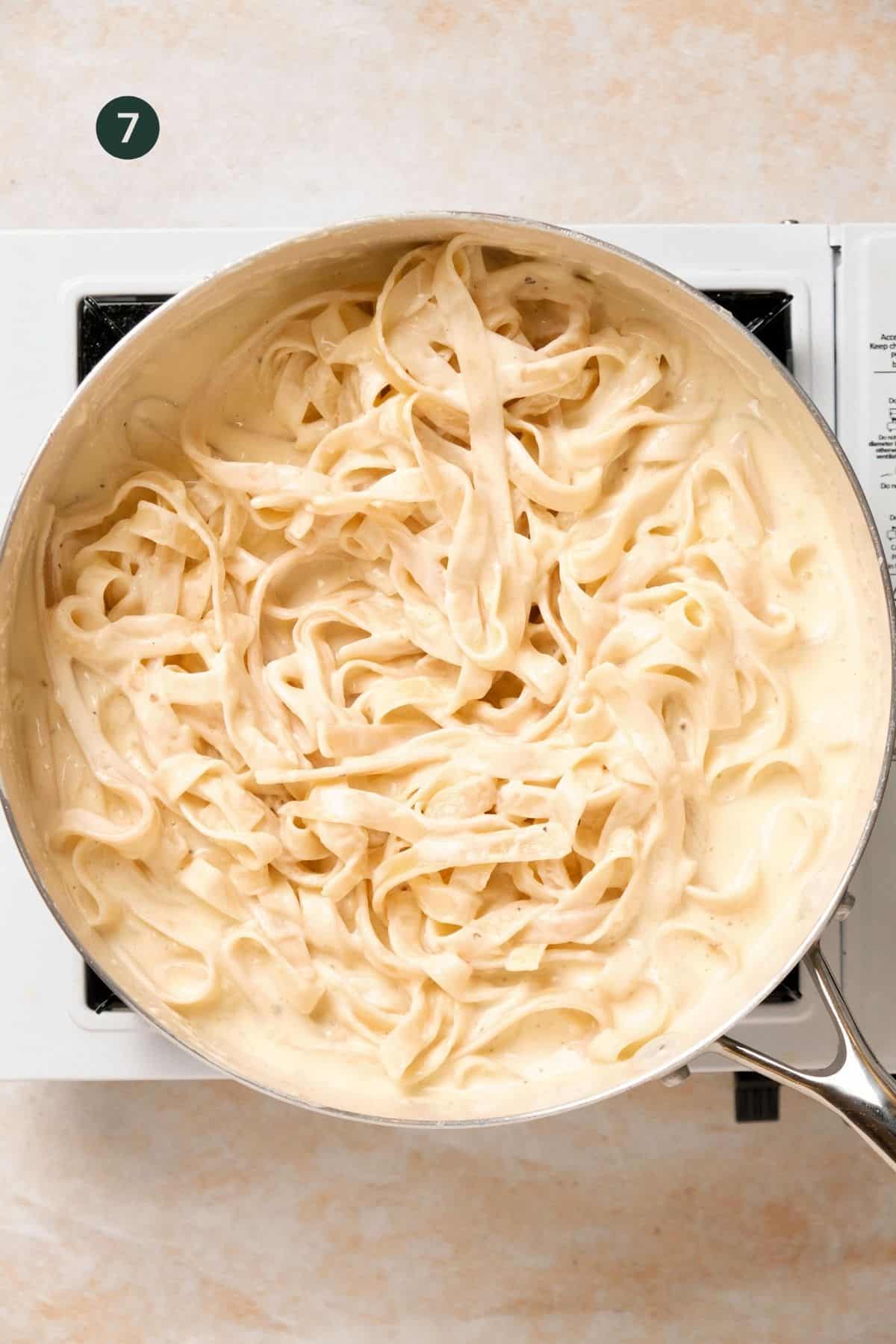 Cooked fettuccine noodles added to alfredo sauce in a skillet.