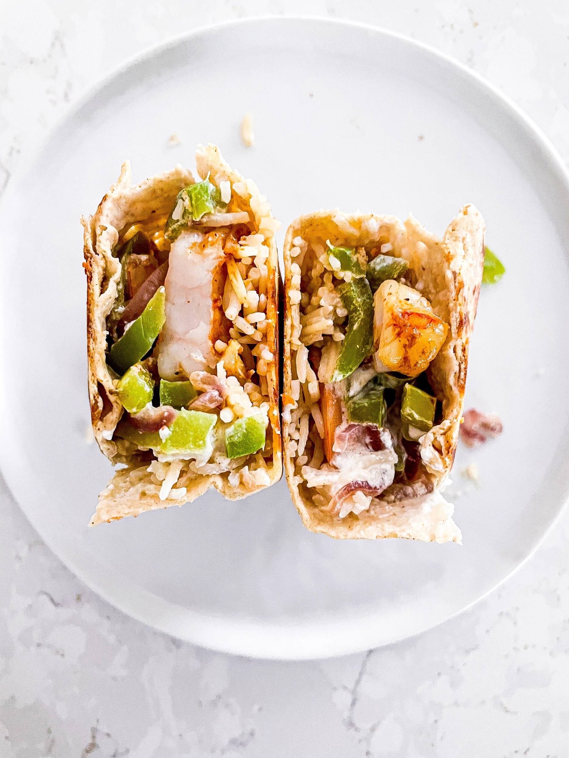 Halved fajita shrimp burrito standing up on a plate.