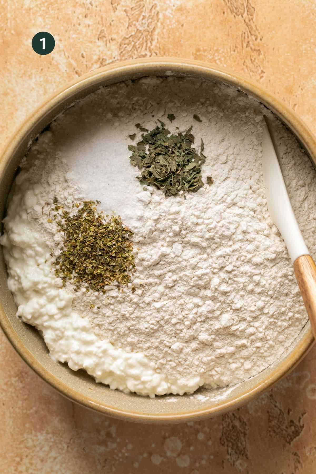 Flour, cottage cheese, salt, oregano and basil added to a bowl to combine.