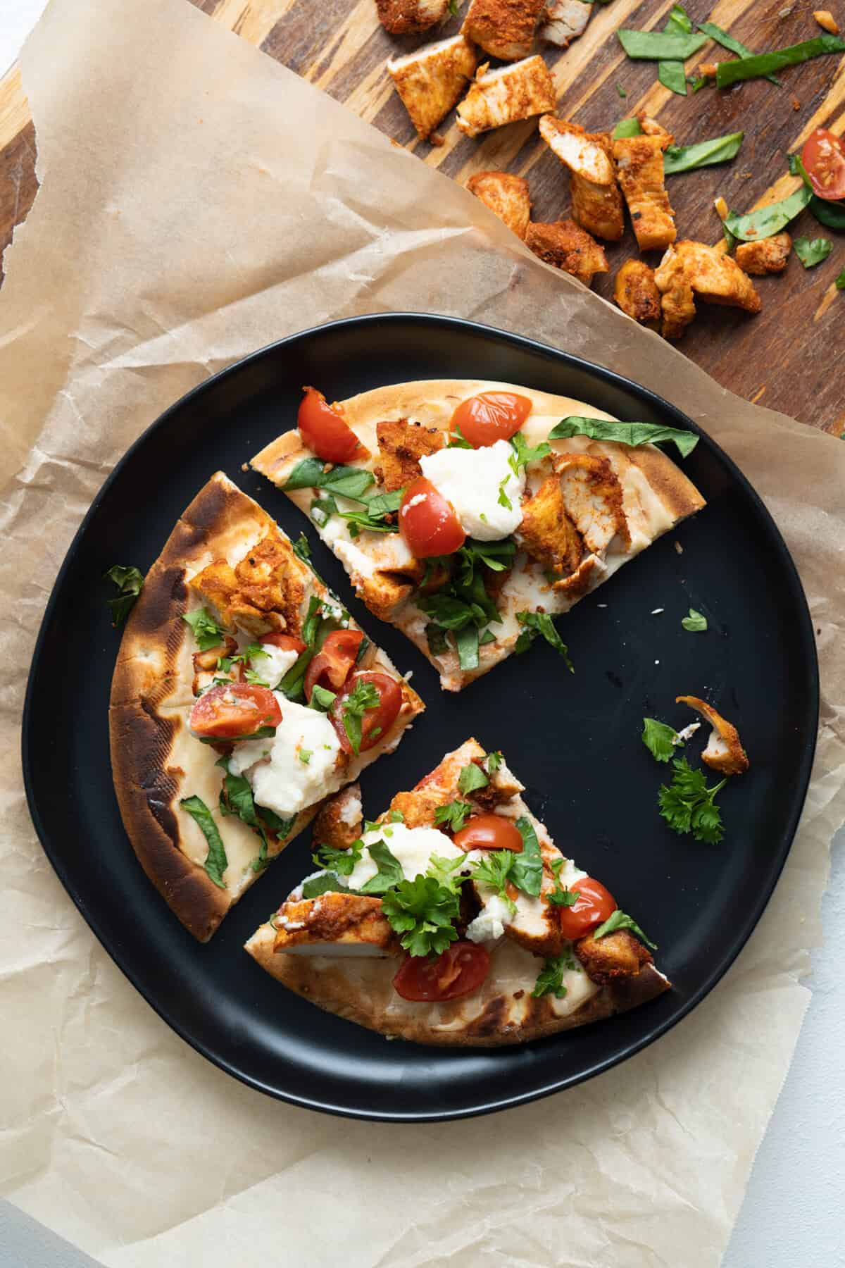 Slices of blackened chicken white sauce pizza on a black plate.