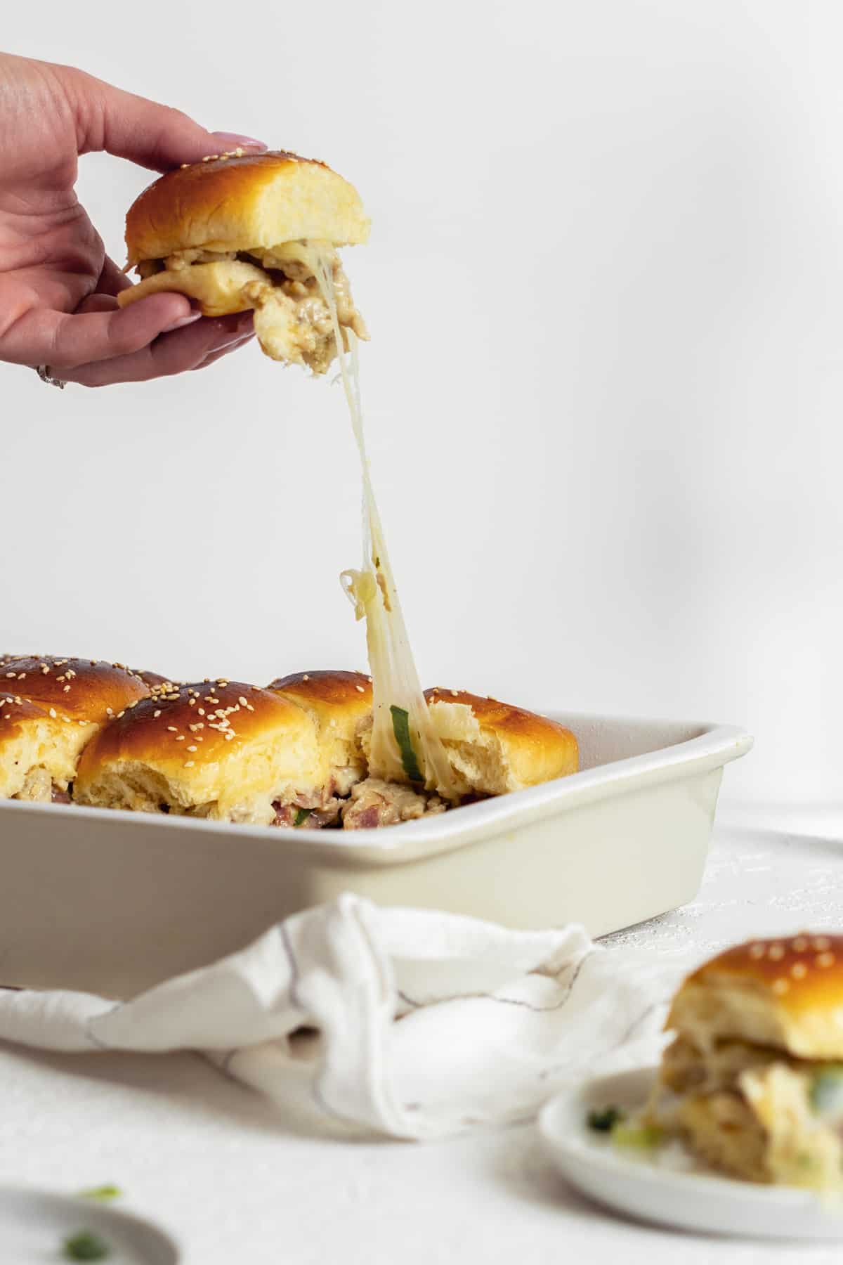Sliders in a baking dish being pulled out with cheese pulling.