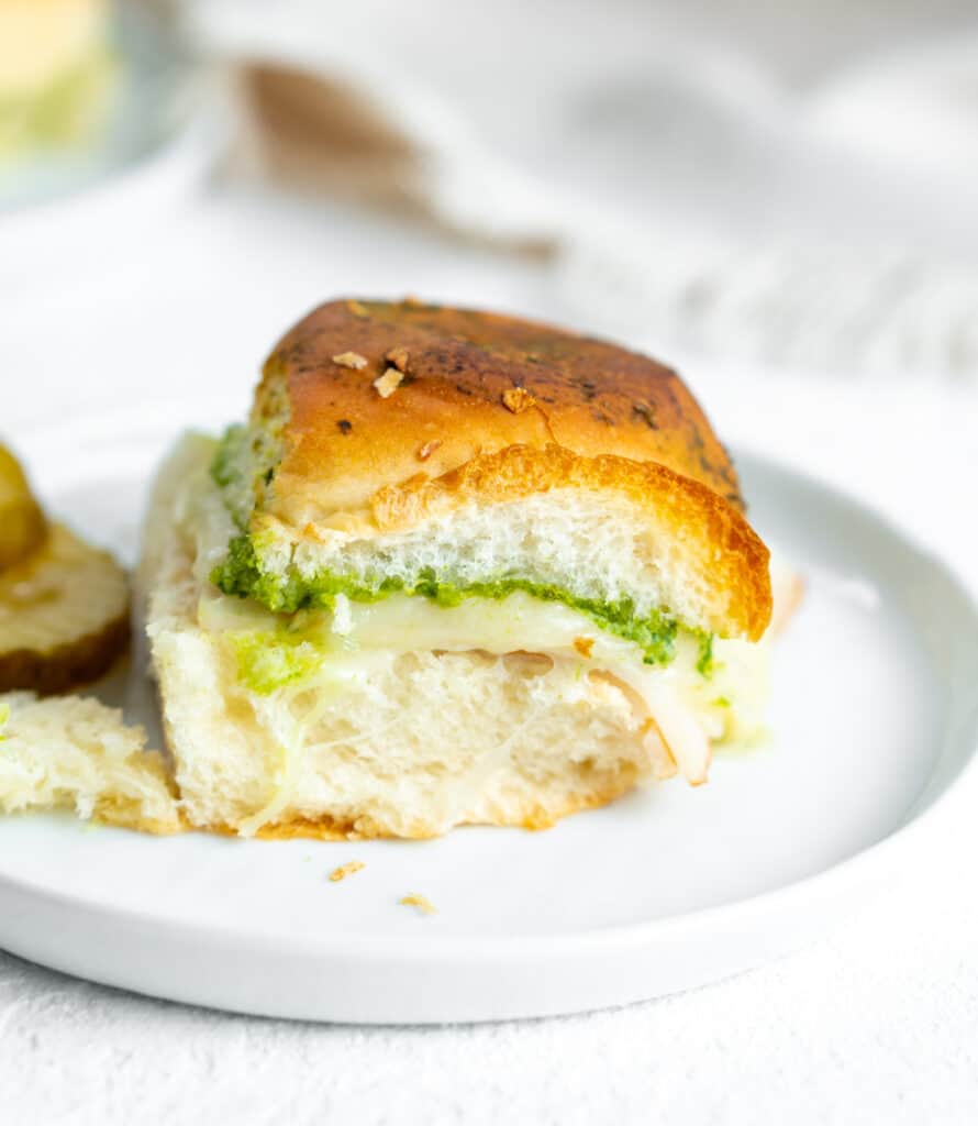 Chicken pesto slider on a white plate with pickle slices.