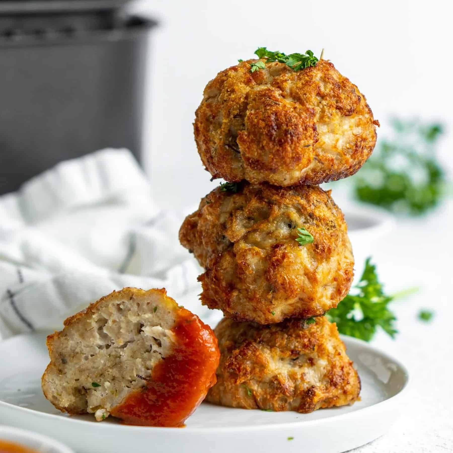 3 stacked air fried meatballs, one cut in half dipped in marinara sauce.