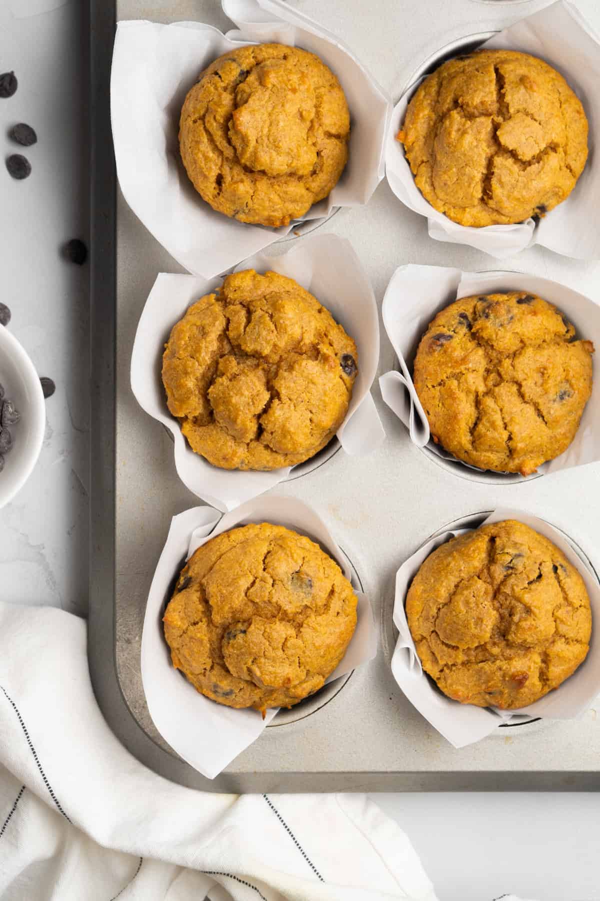 Baked muffins in a muffin pan with liners and chocolate chips off to the side. 