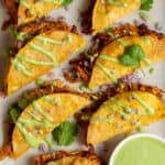 Seven crispy crunchy chicken tacos with a cilantro ricotta sauce for dipping on a sheet pan.