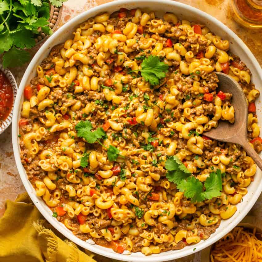 Large bowl of taco mac and cheese with cilantro on top with a wooden spoon ready to serve.