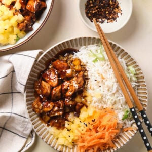 Chopsticks on a bowl with chicken teriyaki, pineapple, carrots, and rice.