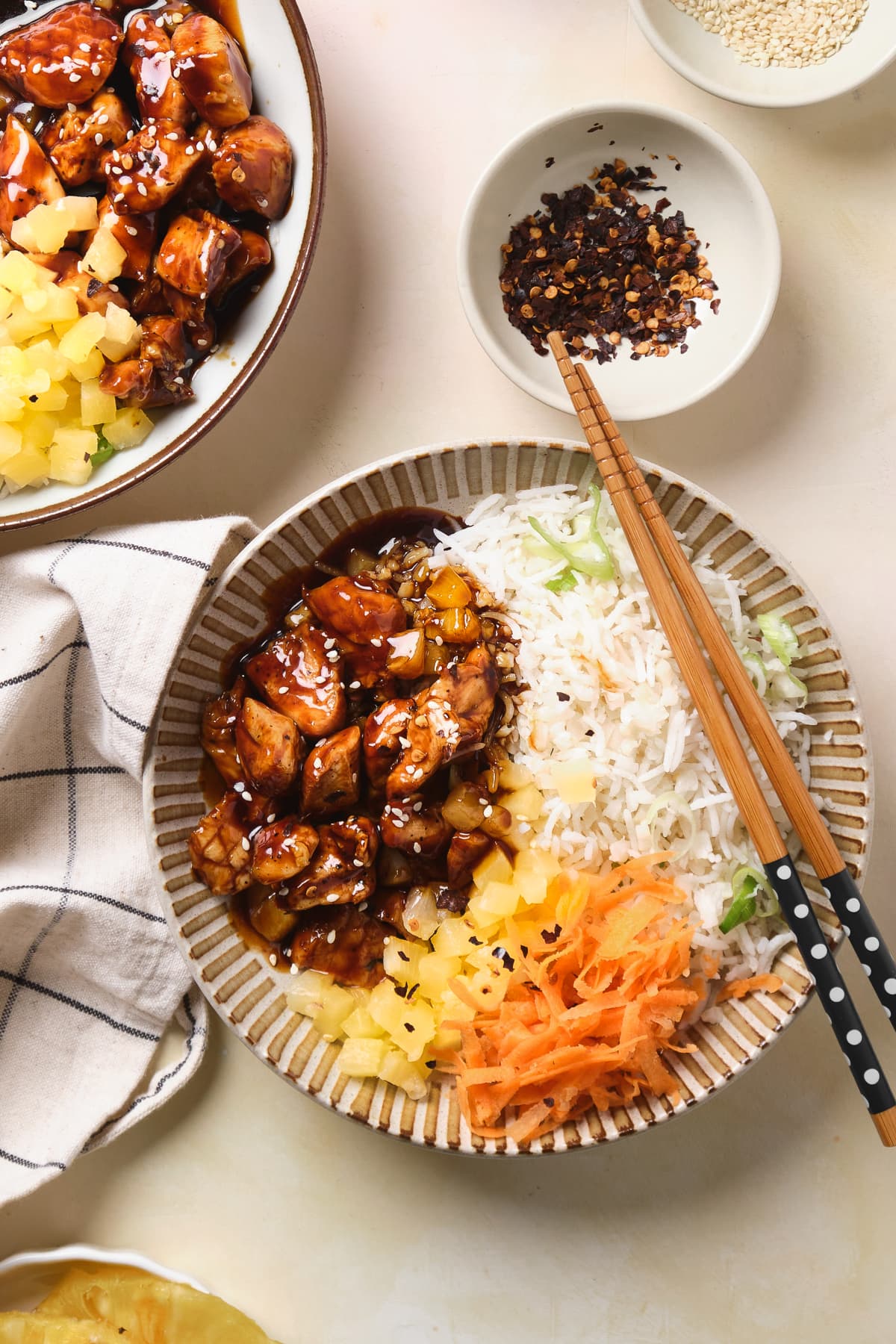 Chopsticks on a bowl with chicken teriyaki, pineapple, carrots, and rice.