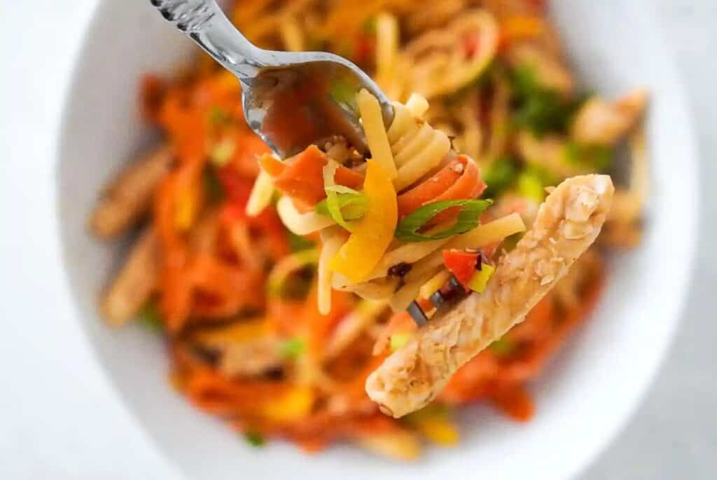 Fork with a bite of peanut chicken noodles.