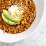 Large bowl of chicken and white bean chili topped with sour cream, cheese, and avocado.