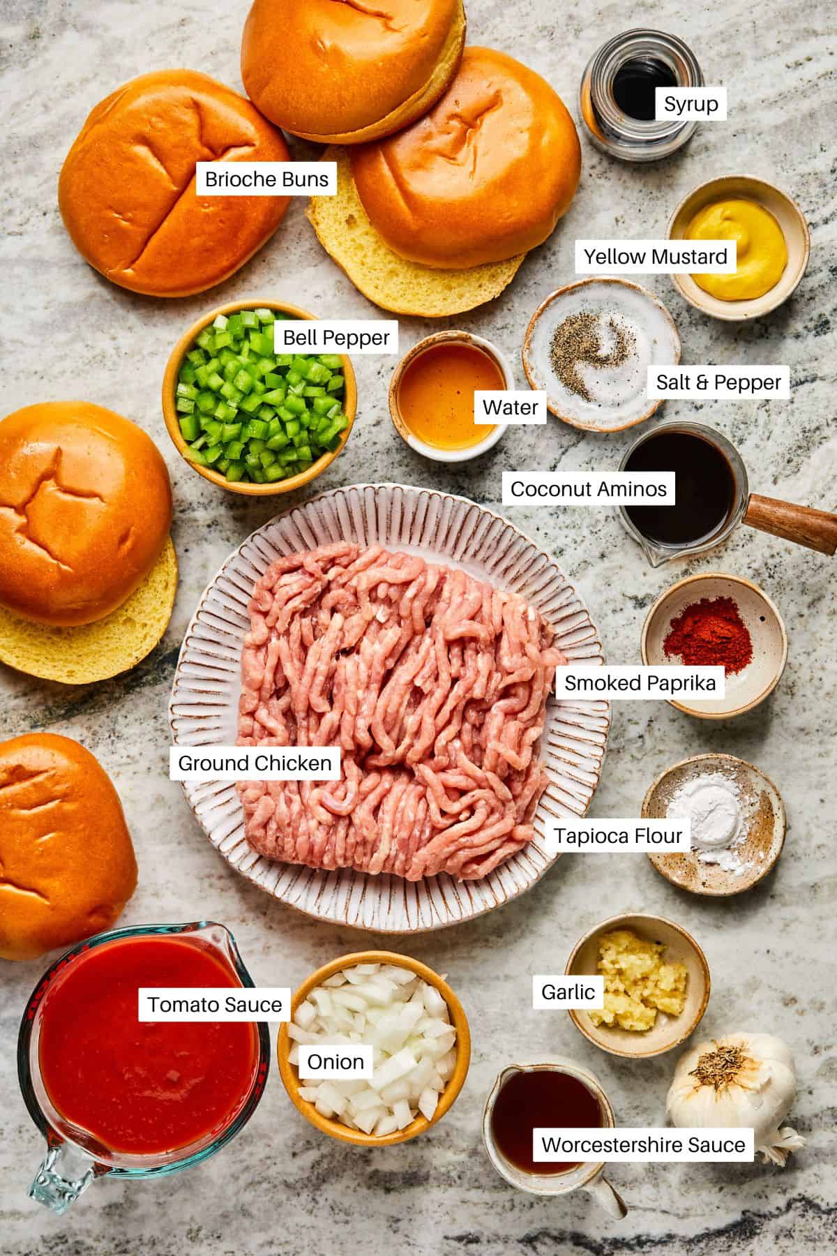 A flat lay image of ingredients for Ground Chicken Sloppy Joes features brioche buns, ground chicken, tomato sauce, diced onion and green bell pepper, garlic, Worcestershire sauce, smoked paprika, mustard, tapioca flour, coconut aminos, and seasonings.