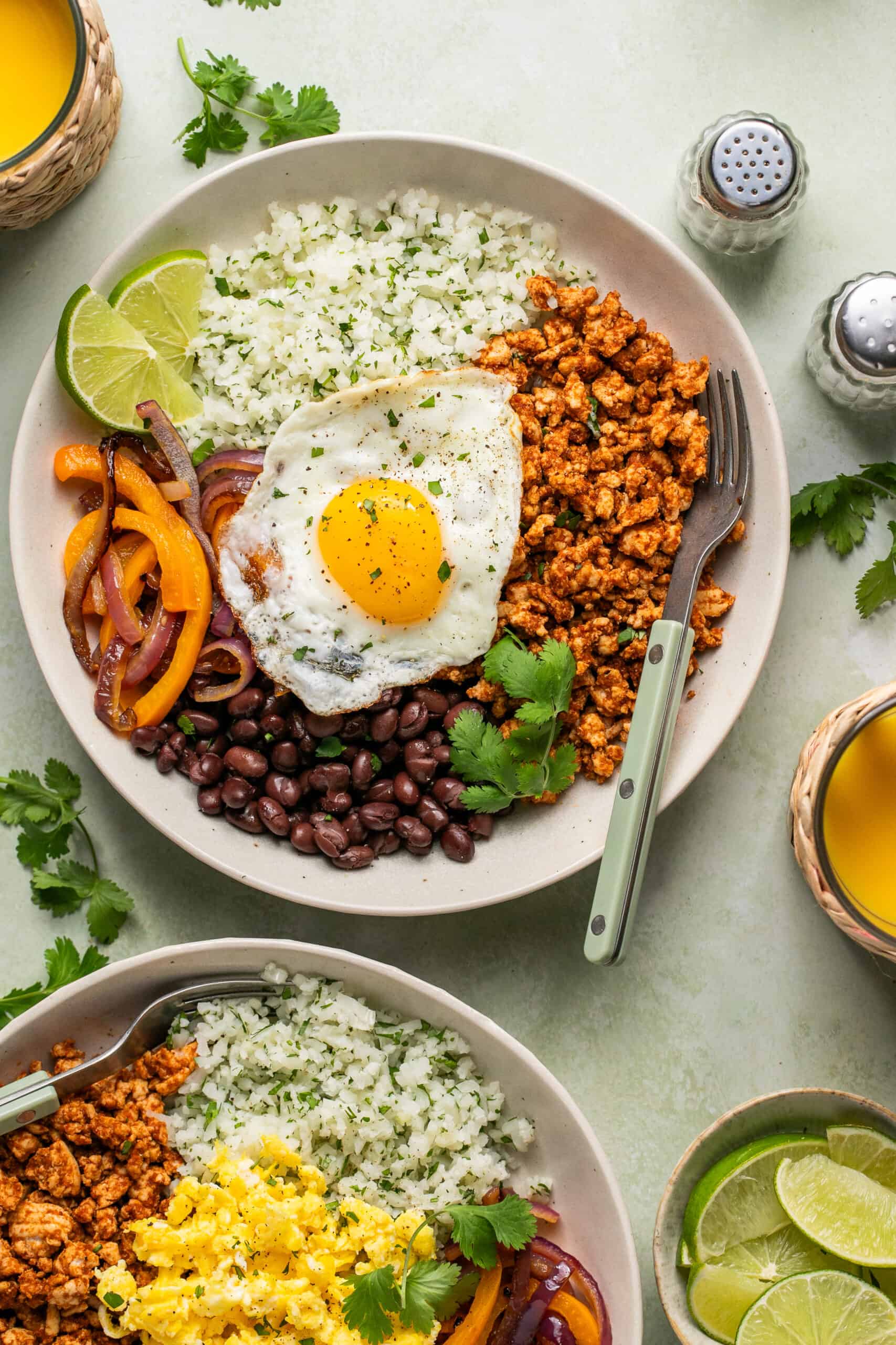 Breakfast bowl full of beans, veggies, cilantro, cauliflower rice and a fried egg on top.