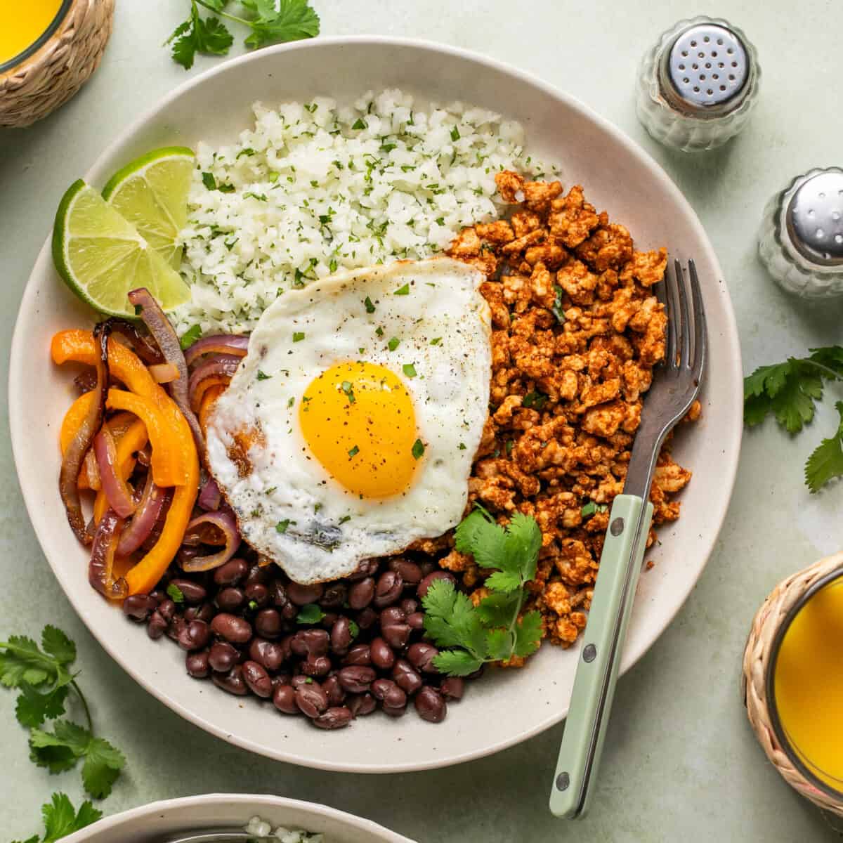 Breakfast bowl full of beans, veggies, cilantro, cauliflower rice and a fried egg on top.