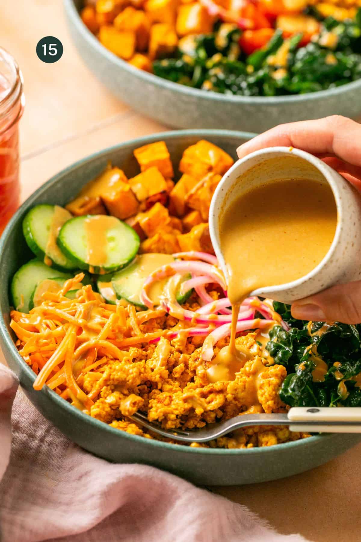 Assembled ground turkey bowls with kale, pickled red onions, cucumbers and peanut sauce being poured on top with a hand. 