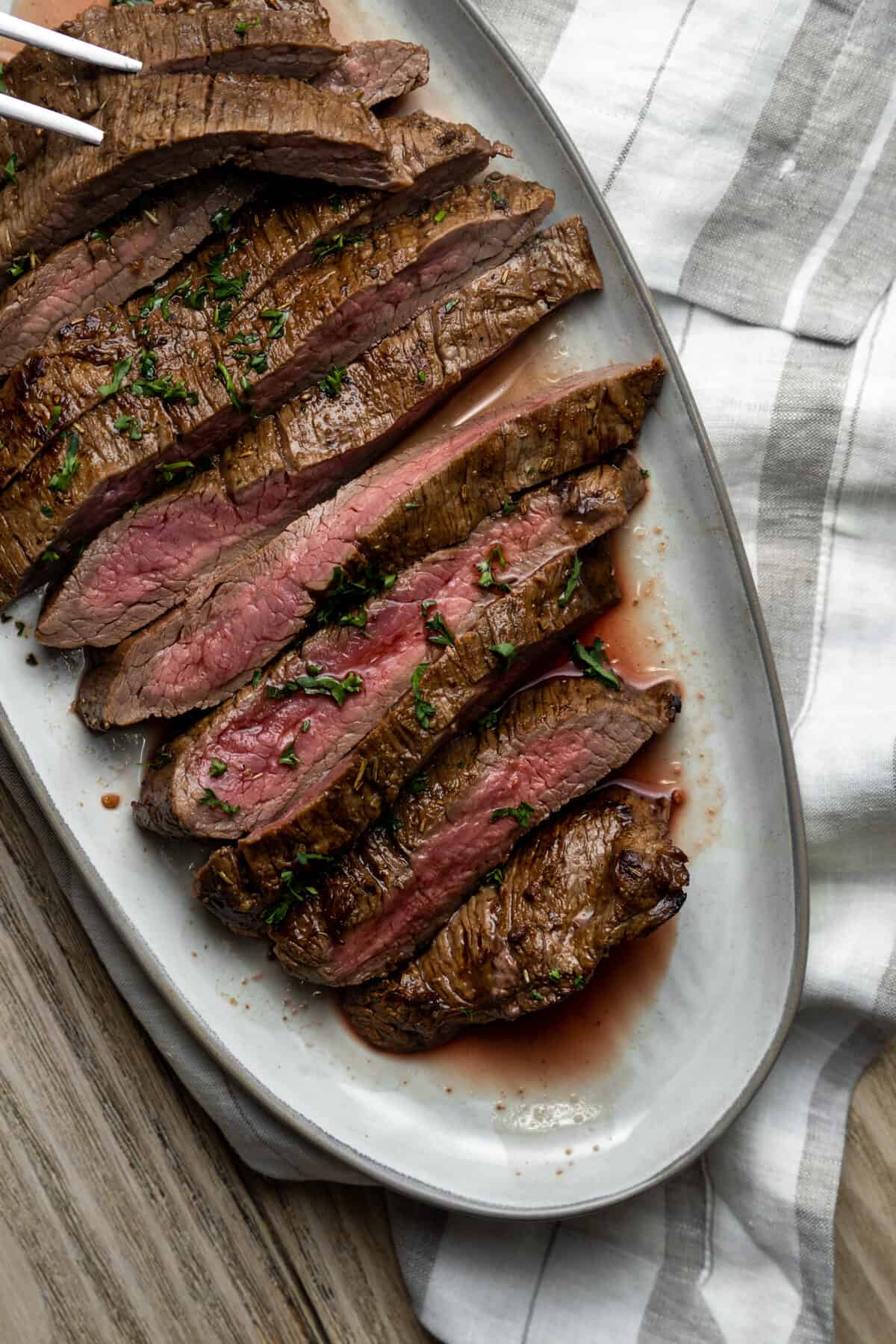 Sliced flank steak on a serving platter with cloth napkins.