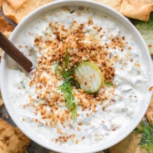 Creamy pickle dip with crunchy breadcrumbs, fresh dill and a pickle on top in a bowl.