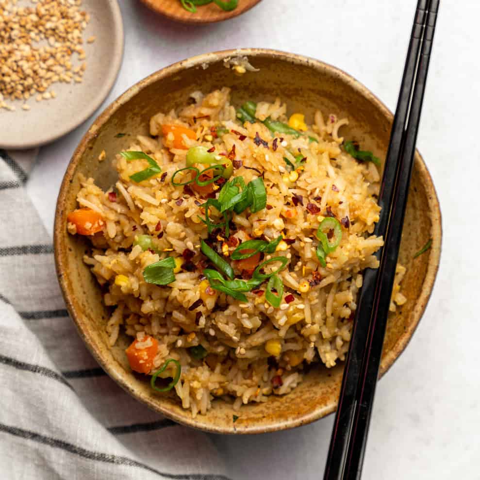 Fried rice in a bowl with chop sticks and topped with sliced green onions.