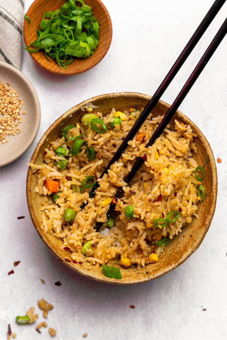 Fried rice in a bowl with chopsticks and topped with green onions. 