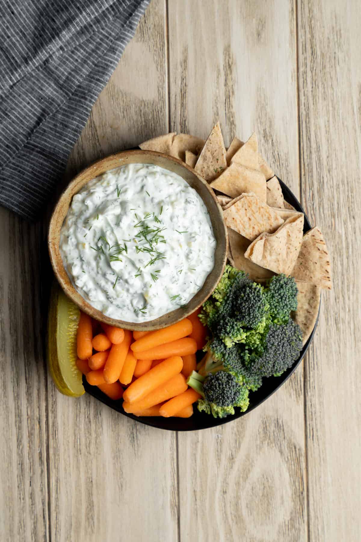 Bowl of dill pickle dip with bread and vegetables for dipping.