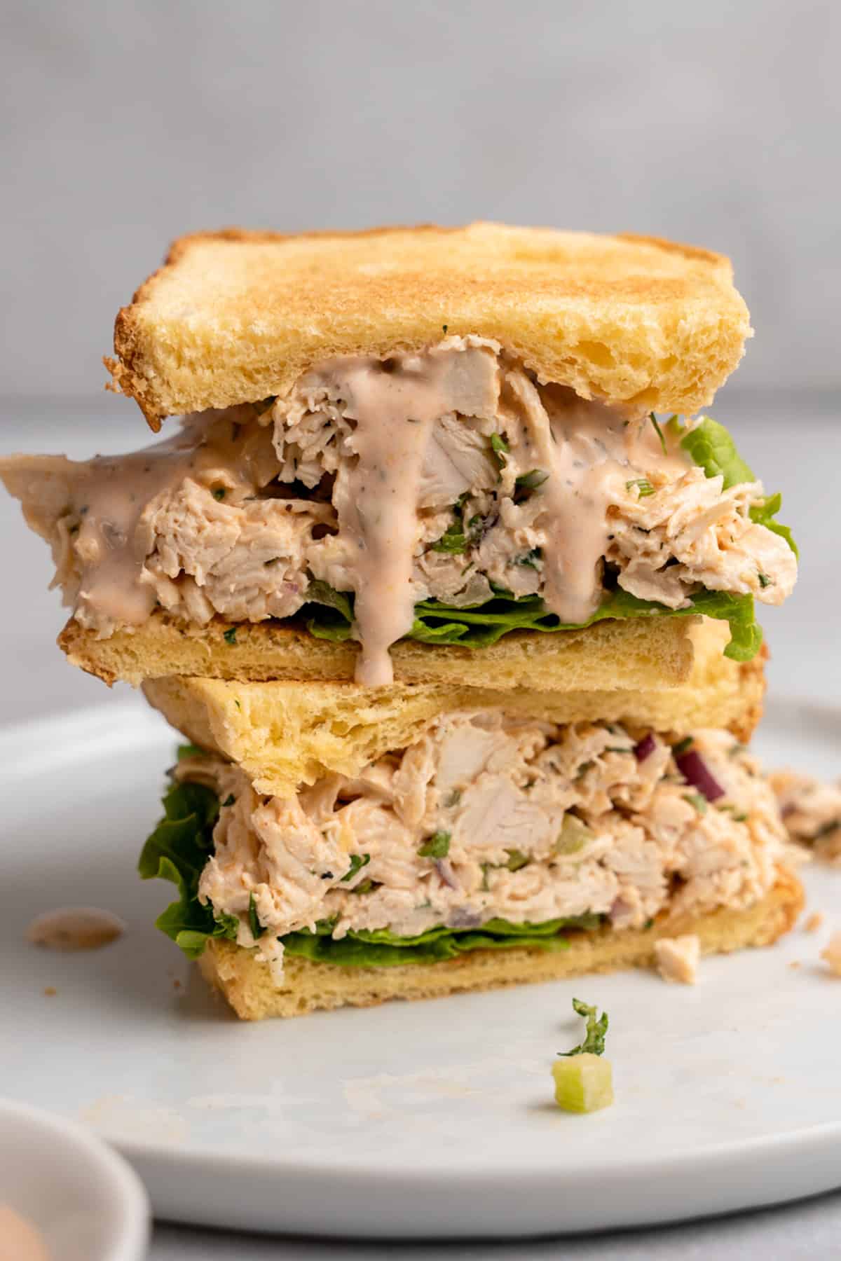 A sandwich stacked with Buffalo Ranch chicken filling, crisp lettuce, and creamy sauce between two slices of toasted bread. It is cut in half and arranged with one piece on top of the other on a white plate.