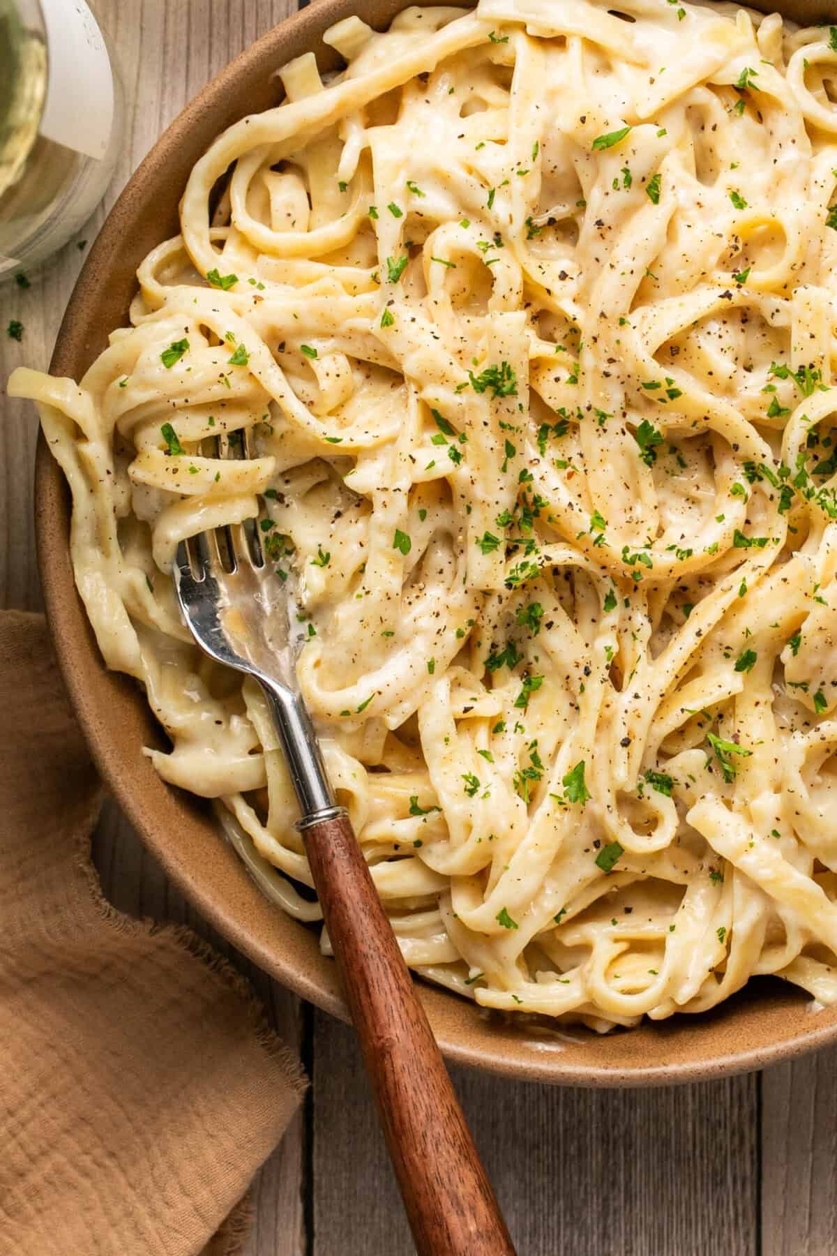 A bowl full of creamy fettucine alfredo topped with fresh parsley and a fork.