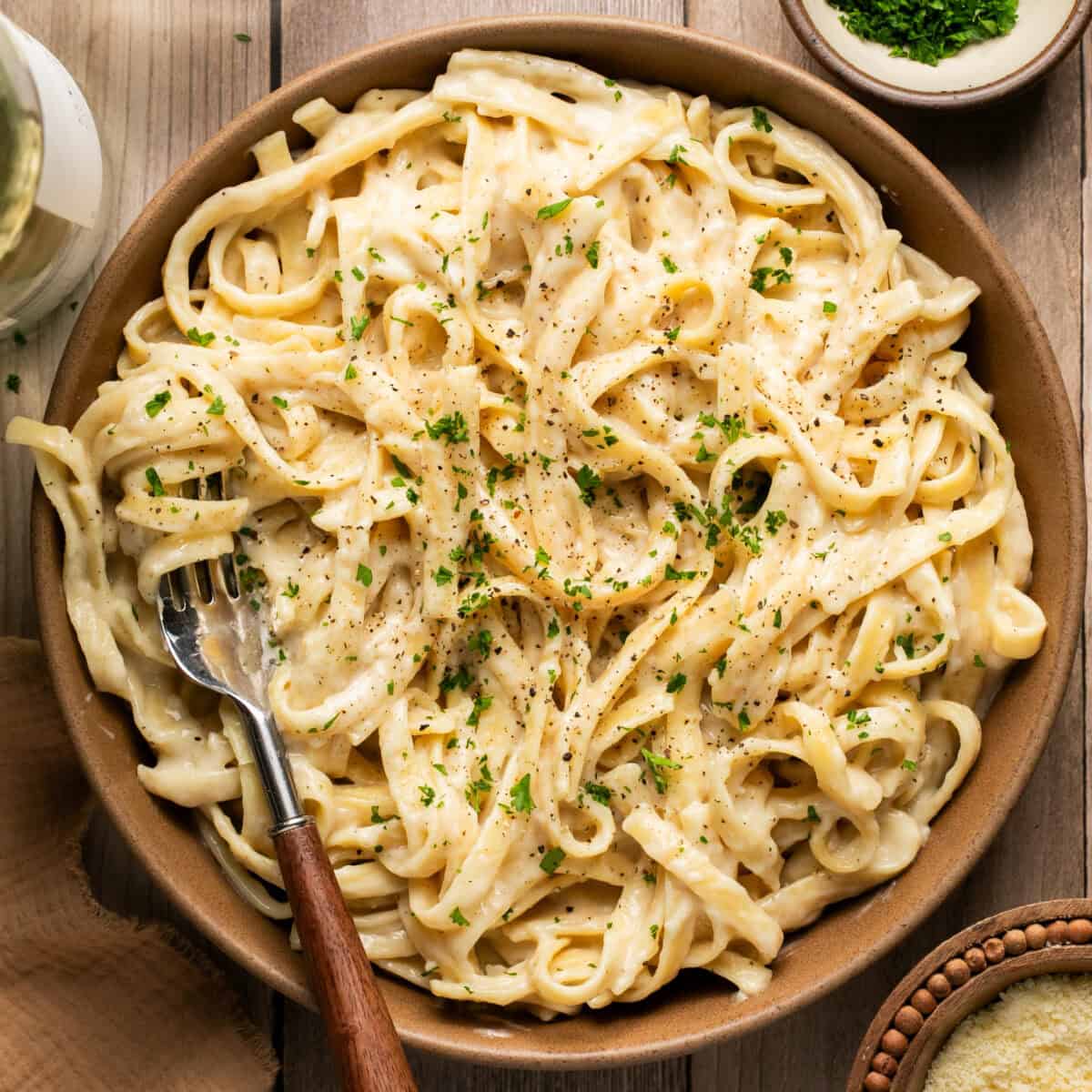 A bowl full of creamy fettucine alfredo topped with fresh parsley.