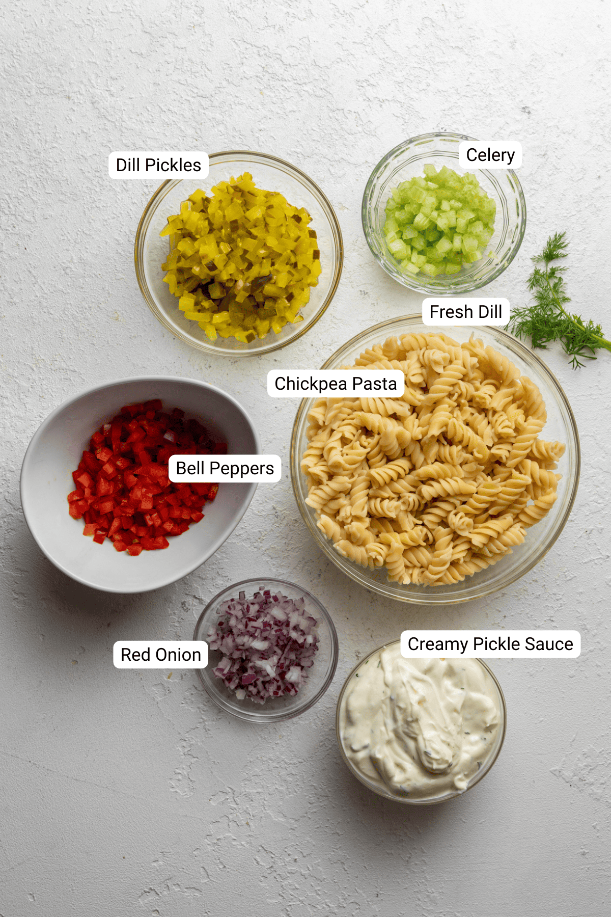Pasta salad ingredients including fresh dill, dill pickles, and creamy pickle sauce.