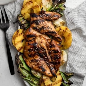 Grilled teriyaki chicken, pineapple, and baby bok choy on a serving platter with a fork.