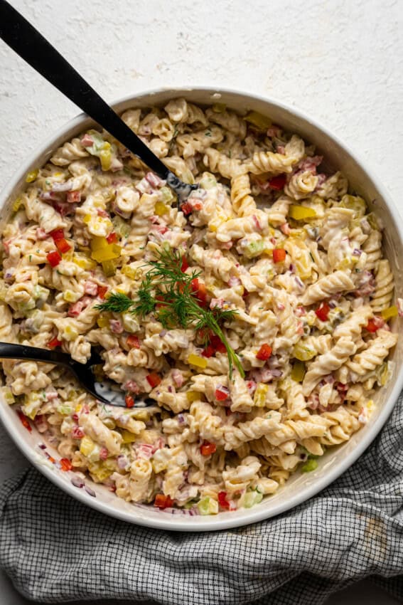 Spoons in a large bowl of dill pickle pasta salad.