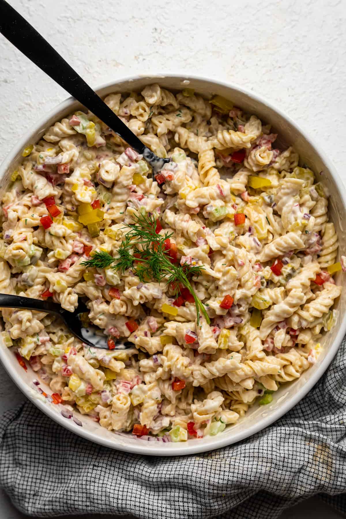 Spoons in a large bowl of dill pickle pasta salad.
