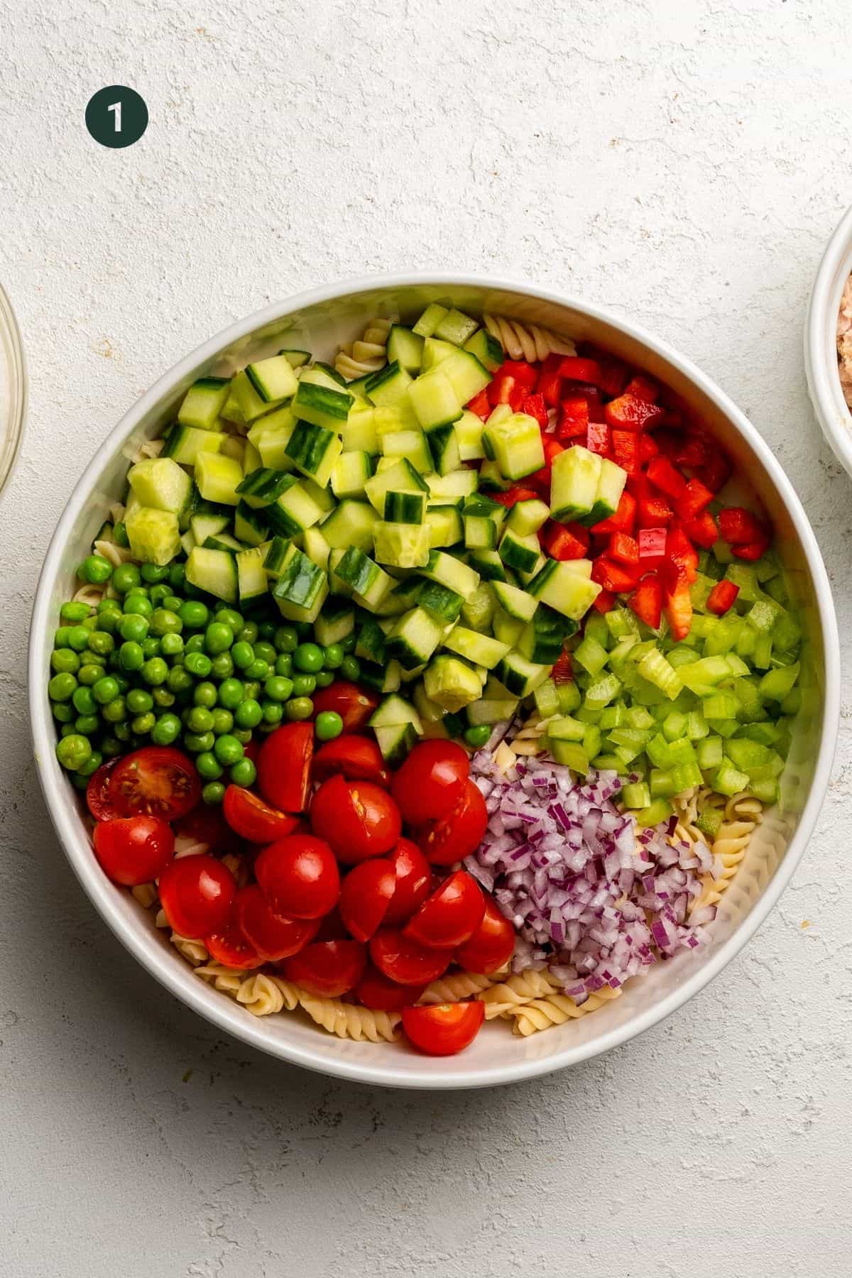 Pasta, tomato, onion, celery, bell pepper. cucumber and peas in a large mixing bowl. 