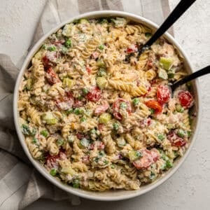 Creamy pasta salad in a large mixing bowl full of fresh vegetables and tuna with serving utensils.
