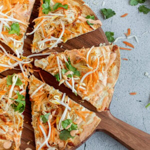 Sliced Thai curry pizza on a wooden pizza board.
