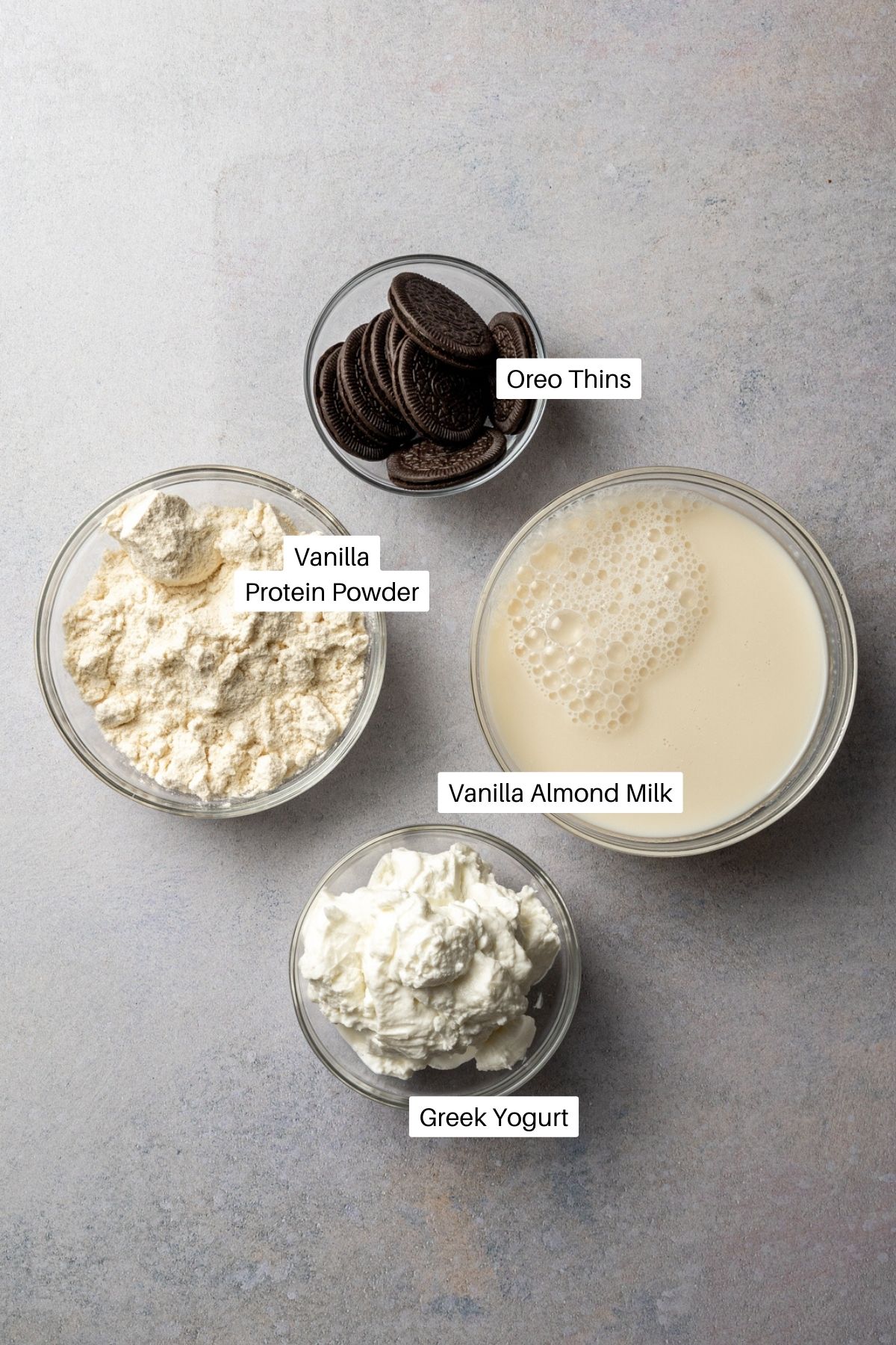Vanilla almond milk, vanilla protein powder, Greek yogurt, and Oreo thins on a counter.