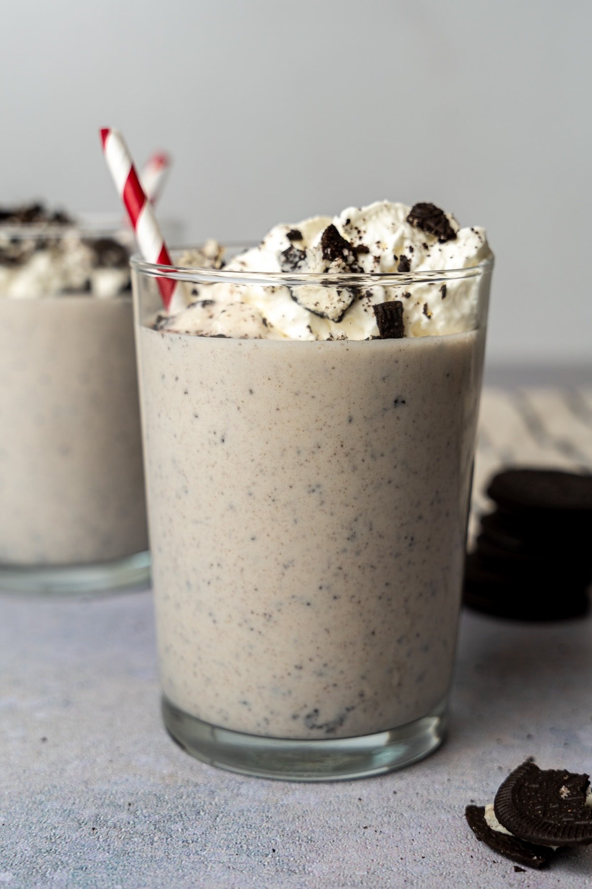 Cookies and cream protein shake with a red and white striped straw in a glass.