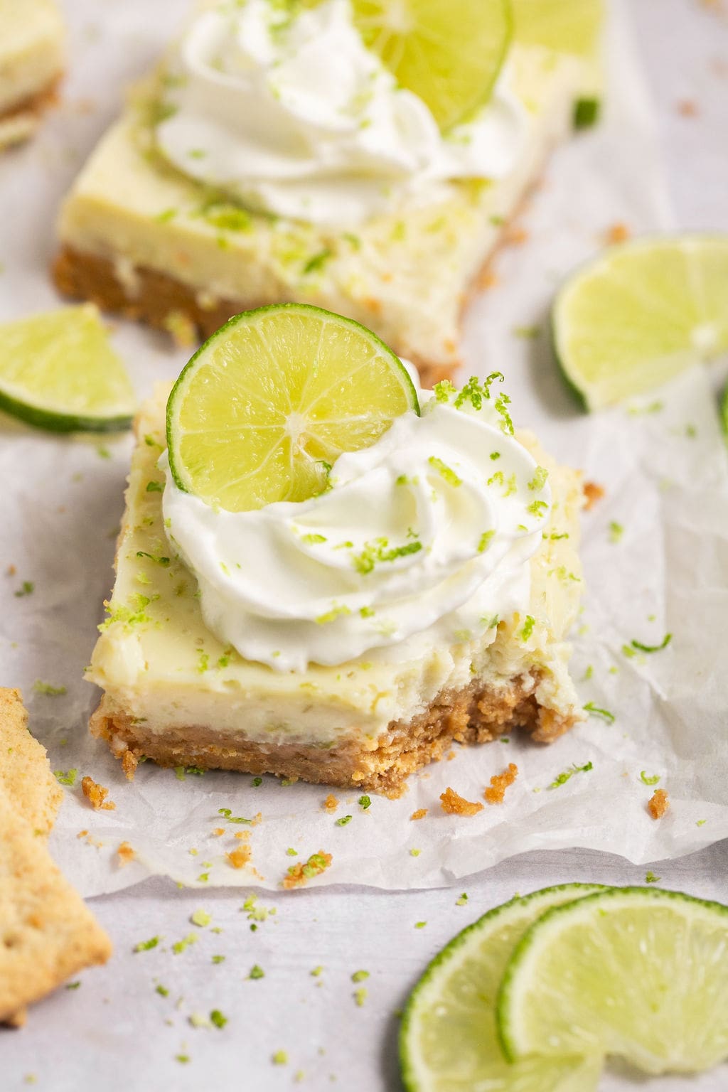 Key lime pie bars on parchment paper, one of which is missing a bite.
