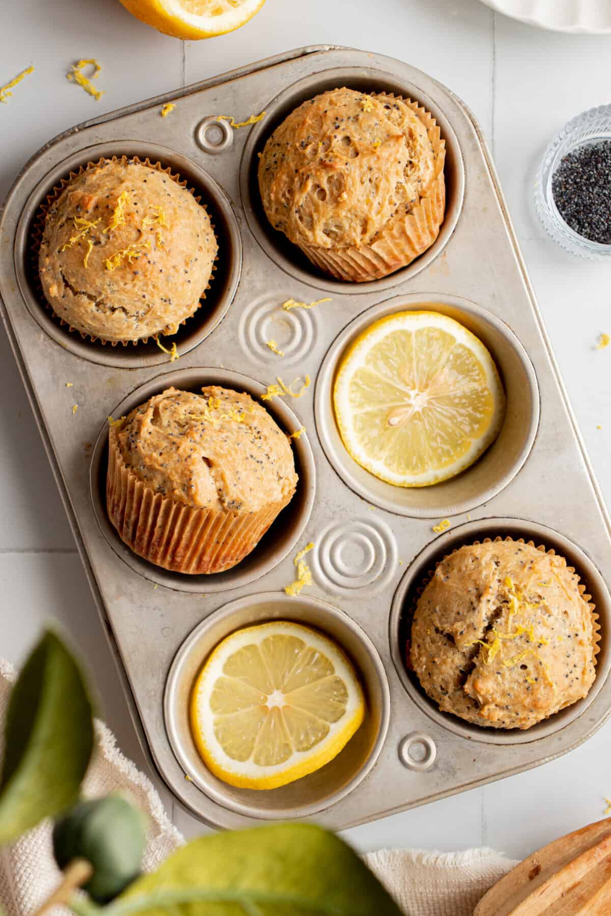 Lemon slices and lemon poppyseed muffins in a muffin tin.