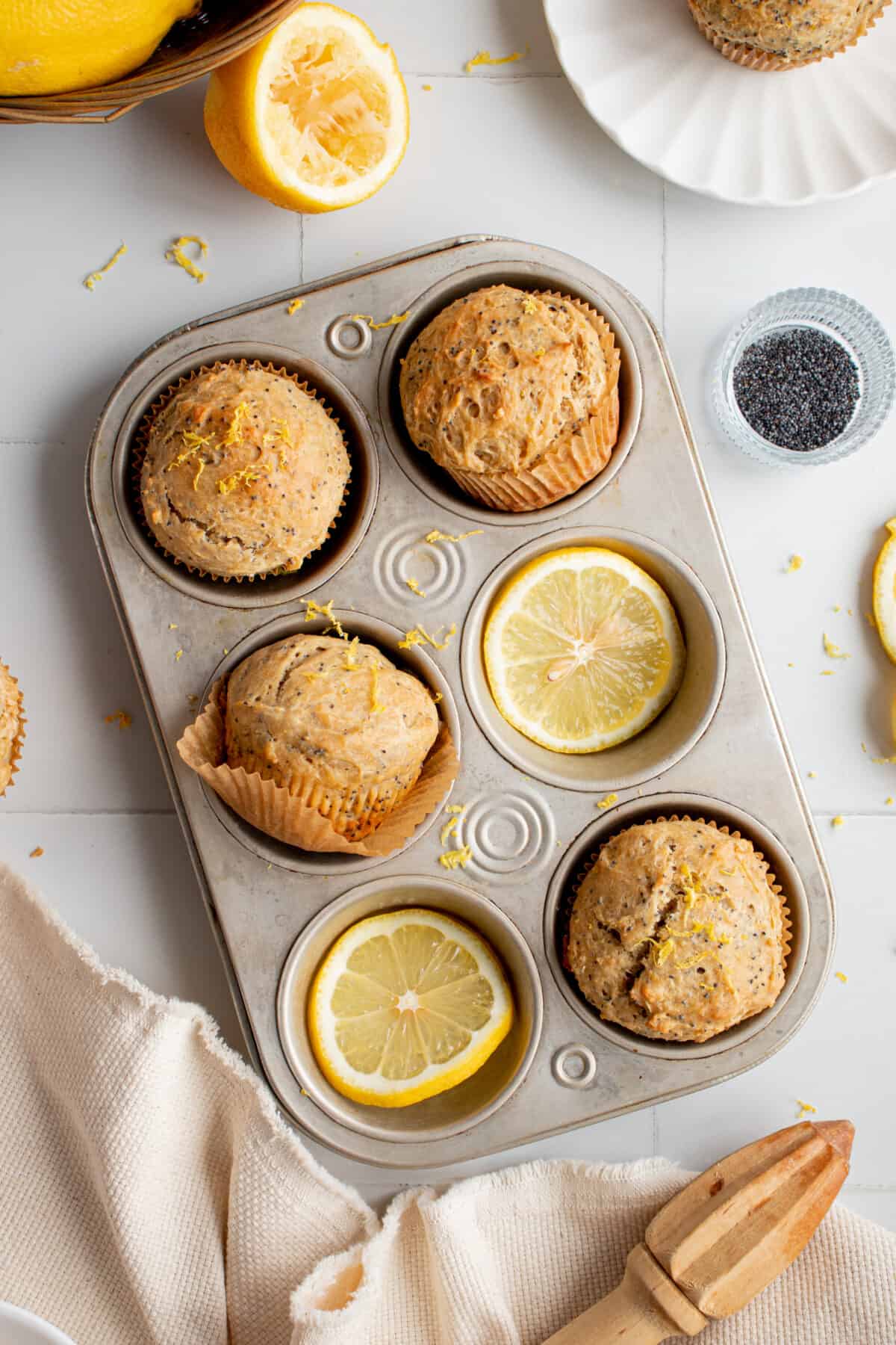 Lemon poppyseed muffins in a muffin tin with lemon slices.