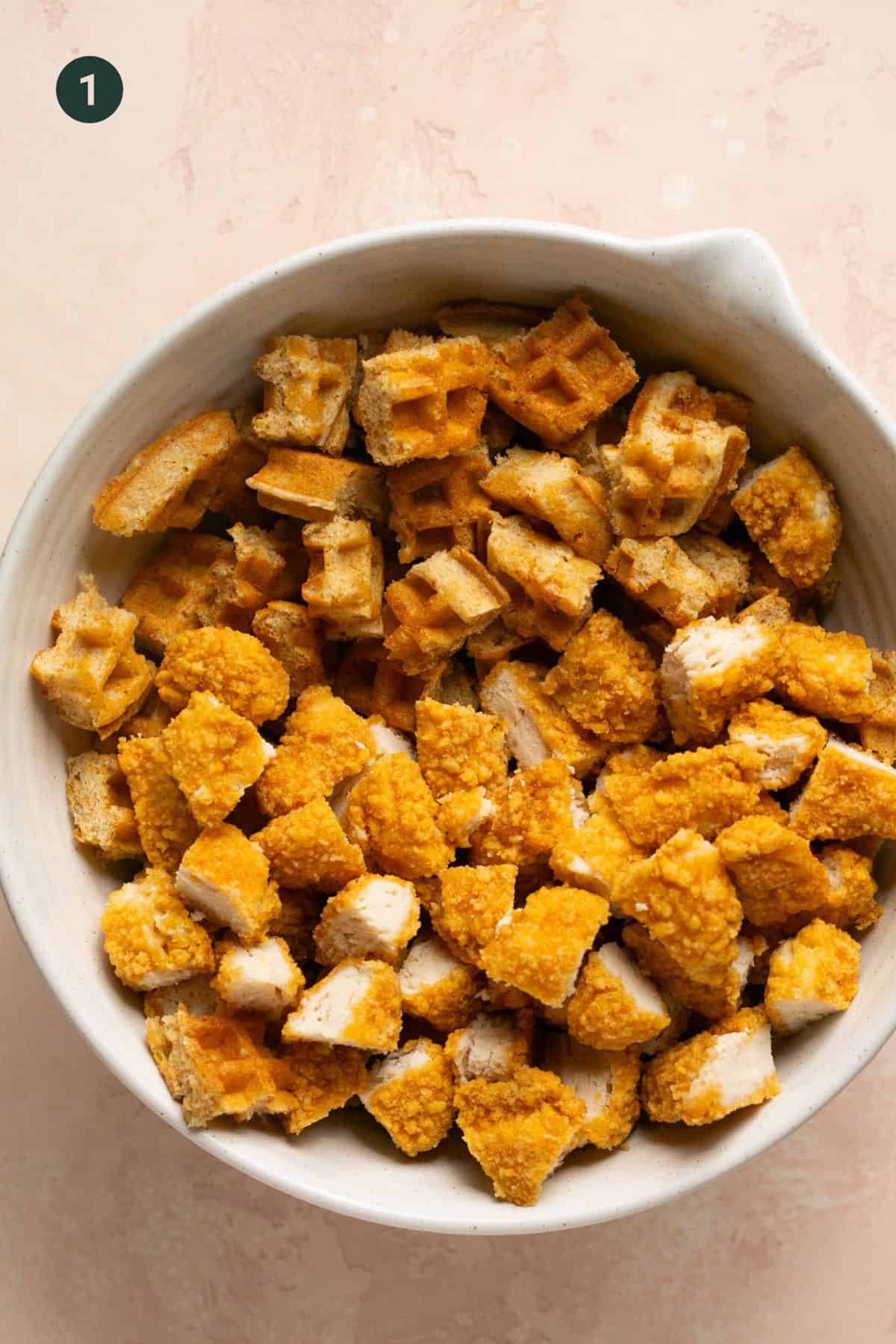 Waffles and chicken nuggets chopped into cubes in a bowl.