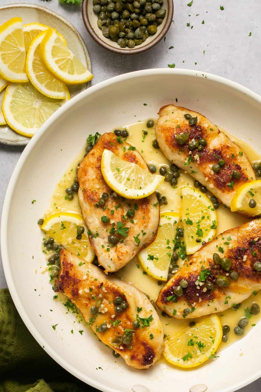 Gluten free chicken piccata on a plate with lemon slices and capers.