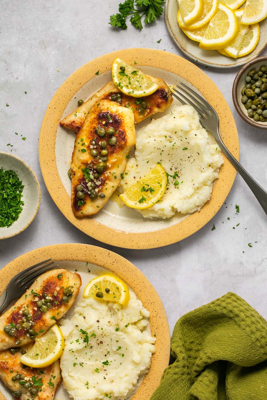 Plates with gluten free chicken piccata on plates with mashed potatoes.