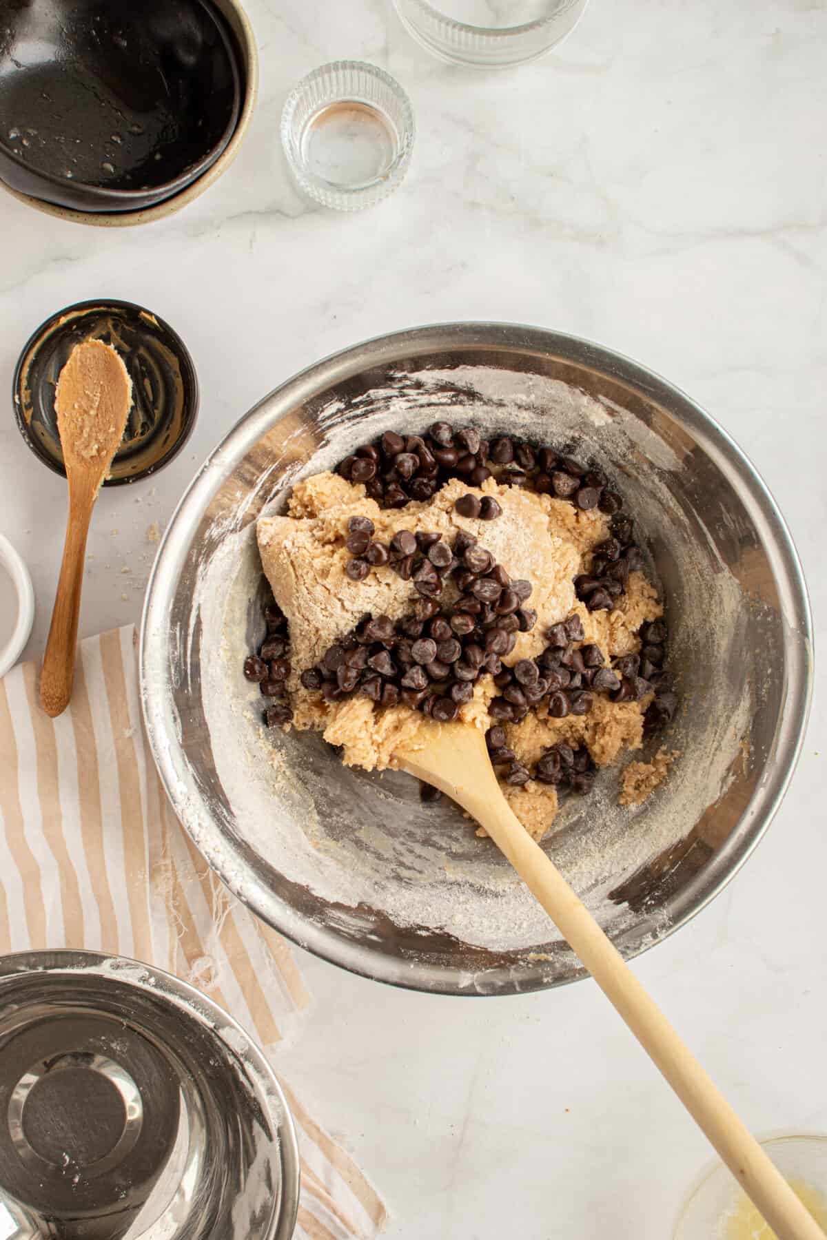 Wooden spoon folding chocolate chips into cookie dough.