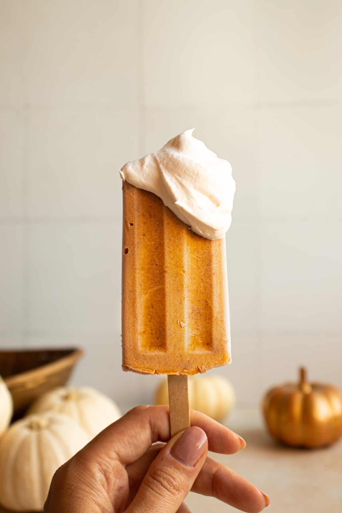 Hand holding pumpkin popsicle with extra cool whip dollop on top. 