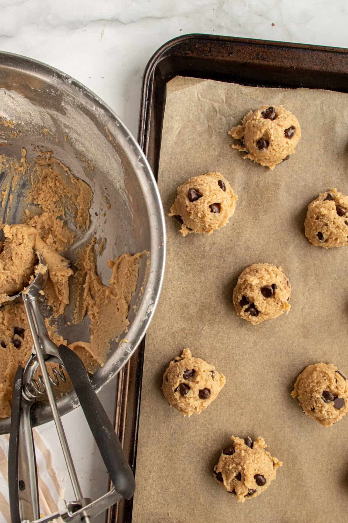 Balls of banana peanut butter chocolate chip cookie dough on a lined baking sheet.