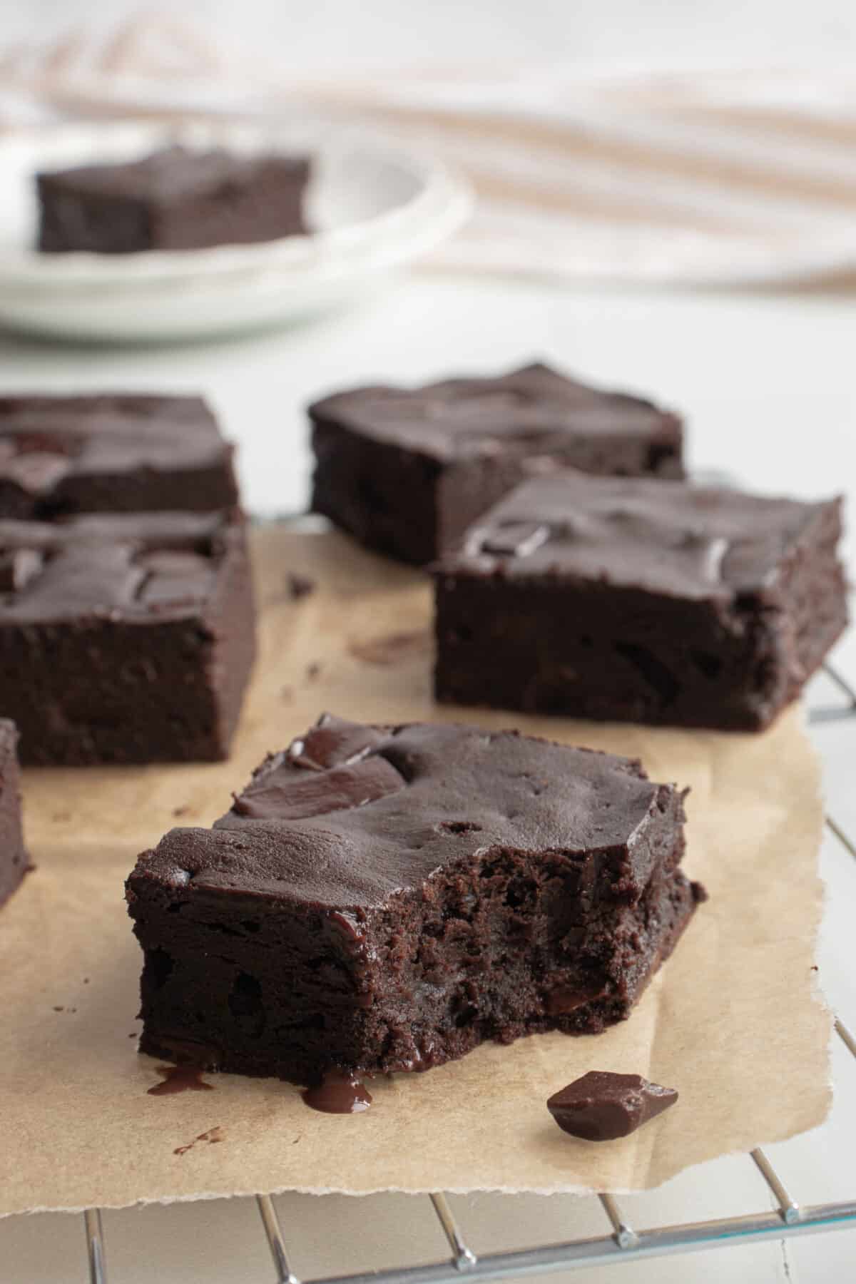 Greek yogurt brownies on parchment paper, one of which is missing a bite.