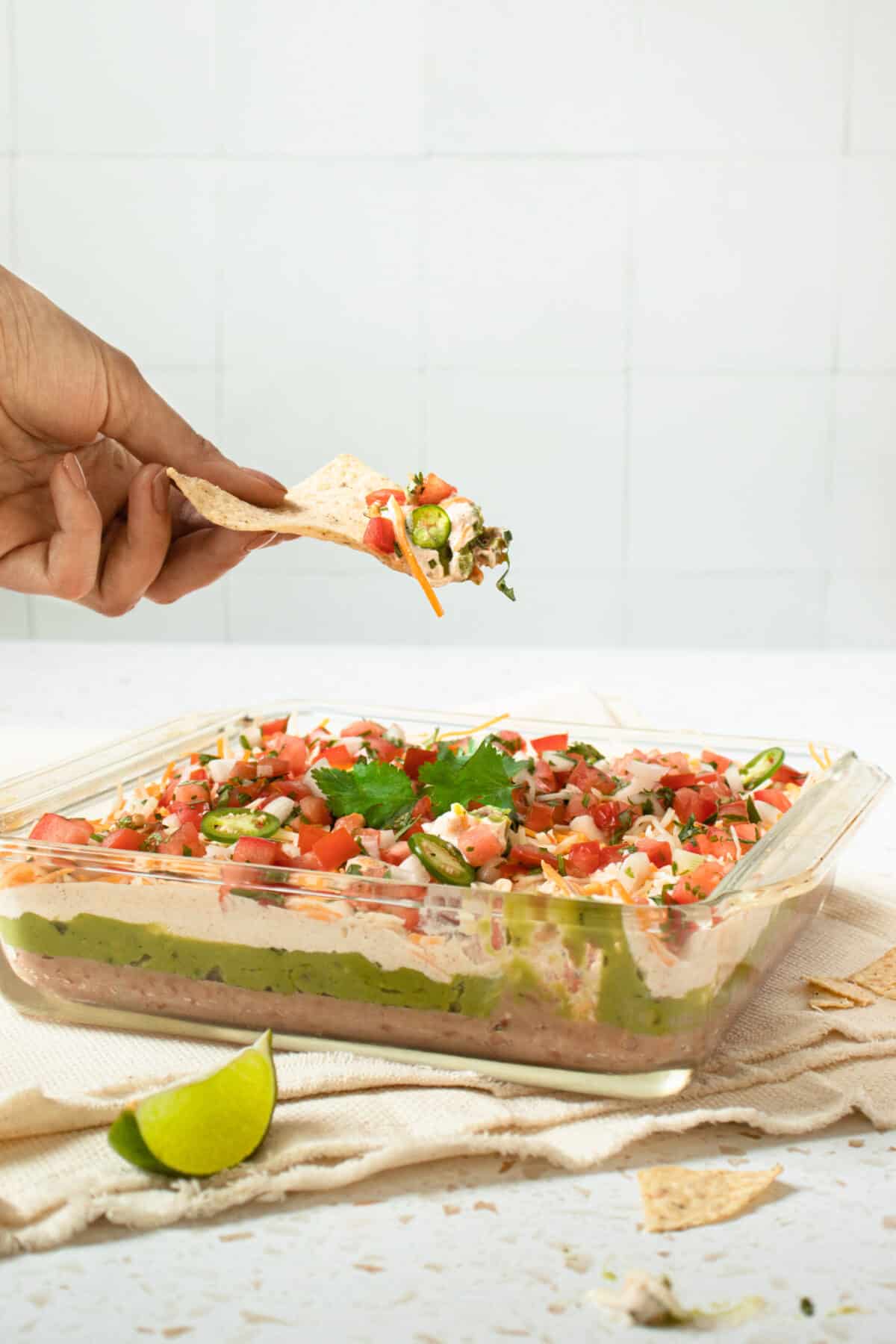 Person scooping five-layer dip with a tortilla chip.